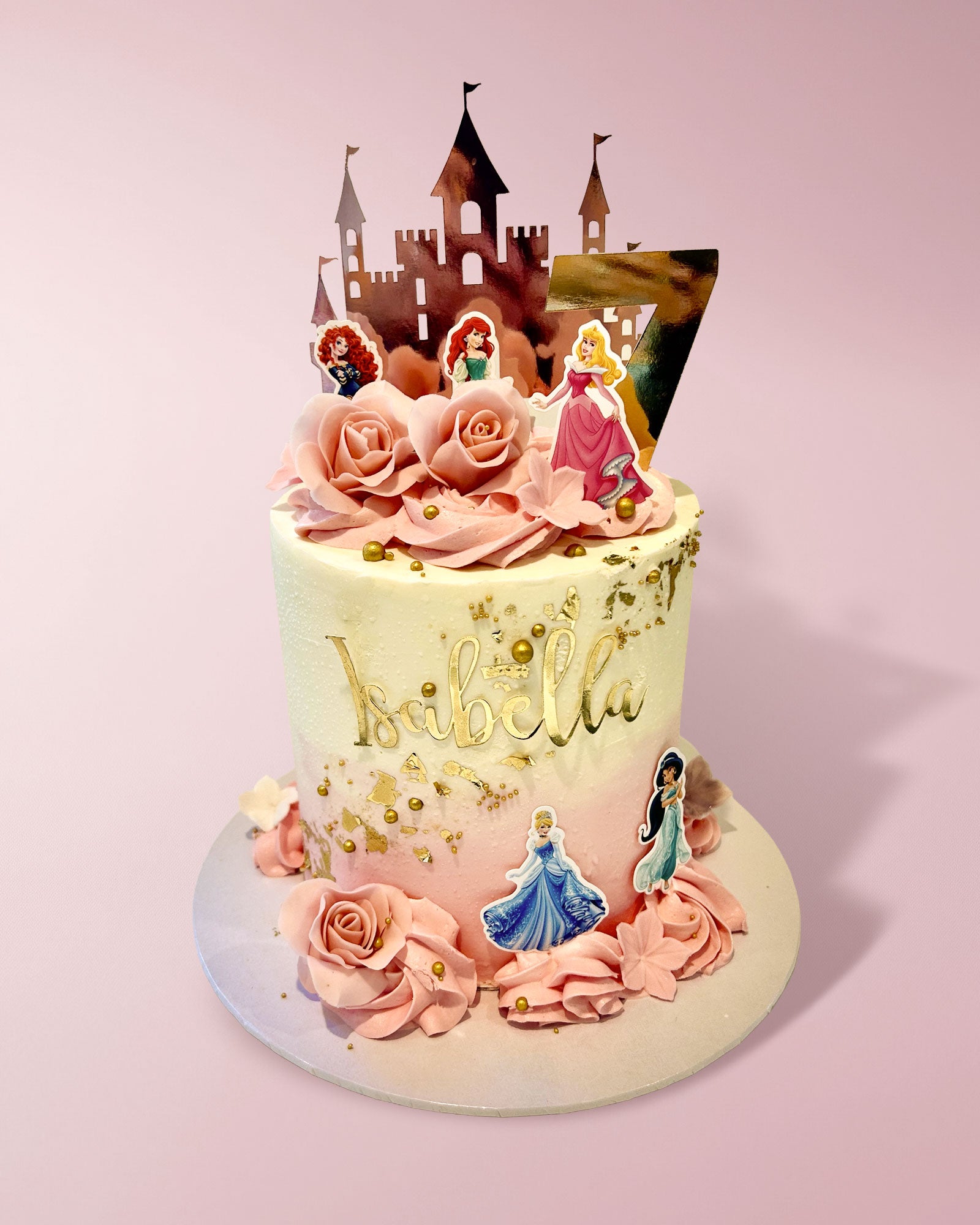 A custom decorated birthday cake with pink frosting roses, gold leaf details, and princess toppers, topped with a castle silhouette on a light pink background.