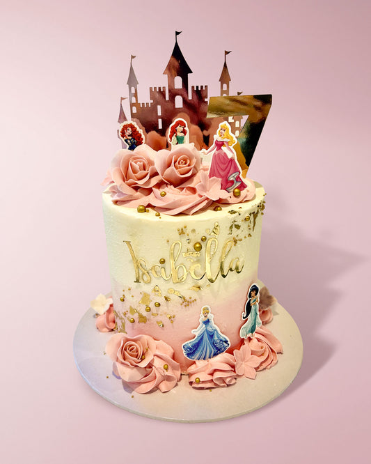A custom decorated birthday cake with pink frosting roses, gold leaf details, and princess toppers, topped with a castle silhouette on a light pink background.
