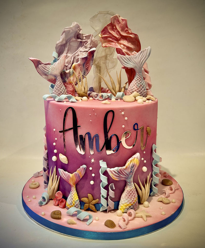 Pink mermaid-themed fondant birthday cake with mermaid tails, seashells, seaweed, edible pearl accents and a wafer sail topper, handmade by Daisy Mud Pie in Brentwood, Essex