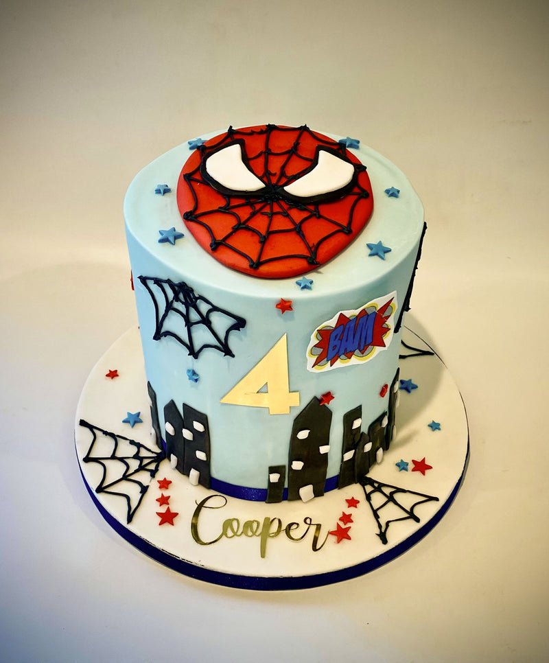 Spider-Man themed fondant birthday cake with light blue frosting, Spider-Man face design, spiderweb detailing, city silhouette and personalised number topper, handmade by Daisy Mud Pie in Brentwood, Essex