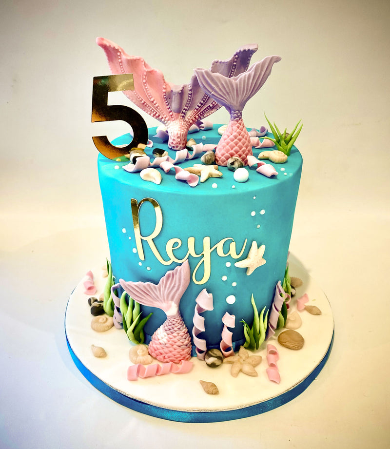 Blue and purple mermaid fondant birthday cake with pink and purple mermaid tails, seashell detailing, gold name icing and gold number topper, handmade by Daisy Mud Pie in Brentwood, Essex