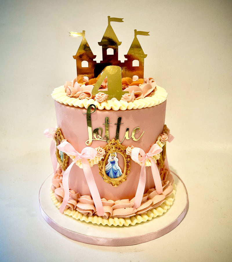 Pink fondant princess castle cake with hand-piped detailing, ribbon trim, gold castle topper and princess-in-the-mirror accents, handmade by Daisy Mud Pie in Brentwood, Essex