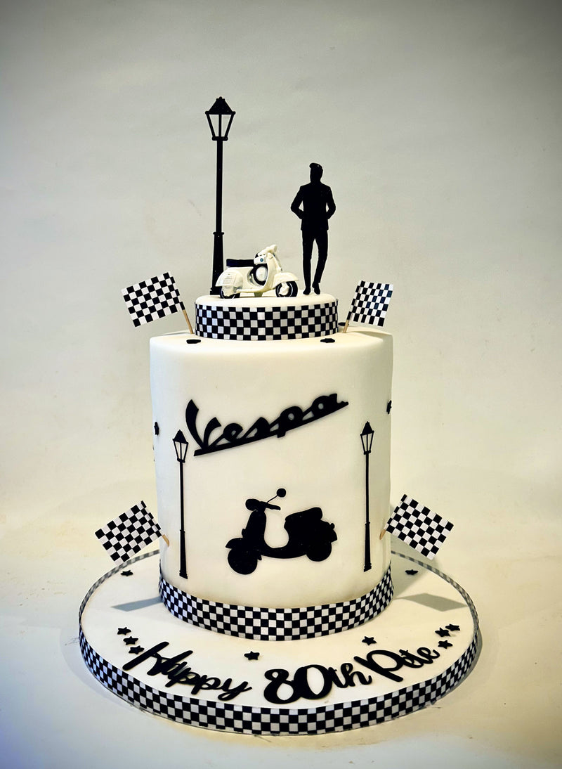 A custom two-tier white cake decorated with black and white checkered patterns, featuring a black scooter, street lamp, and a silhouette of a person on top, with 'Happy 80th Pie' written on the base.